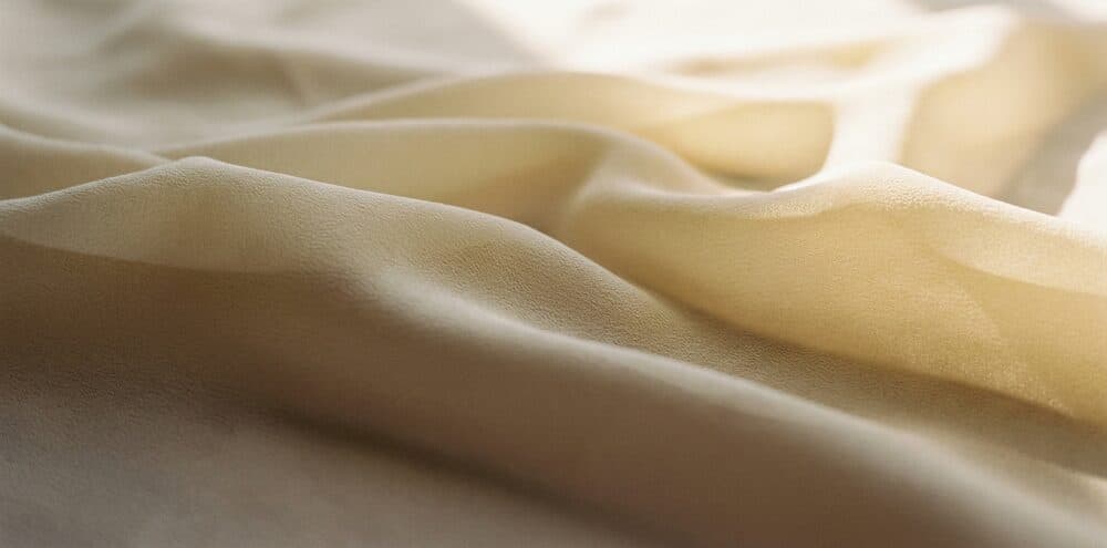Detail of Mysore crepe silk in ivory and pale gold, showing its fine matte crepe texture and liquid drape