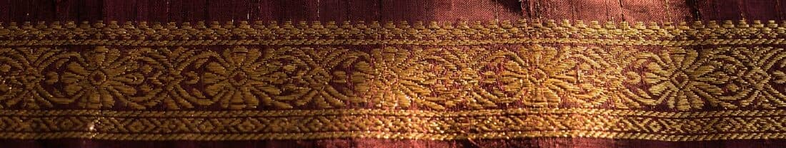 Macro detail of handwoven silk — visible slubs and slight variation in the weft, with a gold zari border interlocked into the body